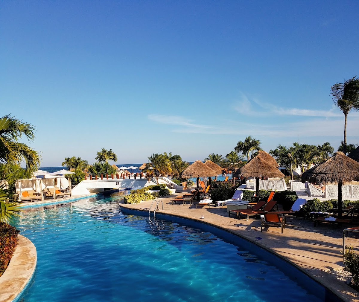 Pool area with lounge chairs, palapas, and ocean view at Moon Palace Cancun under clear blue sky.