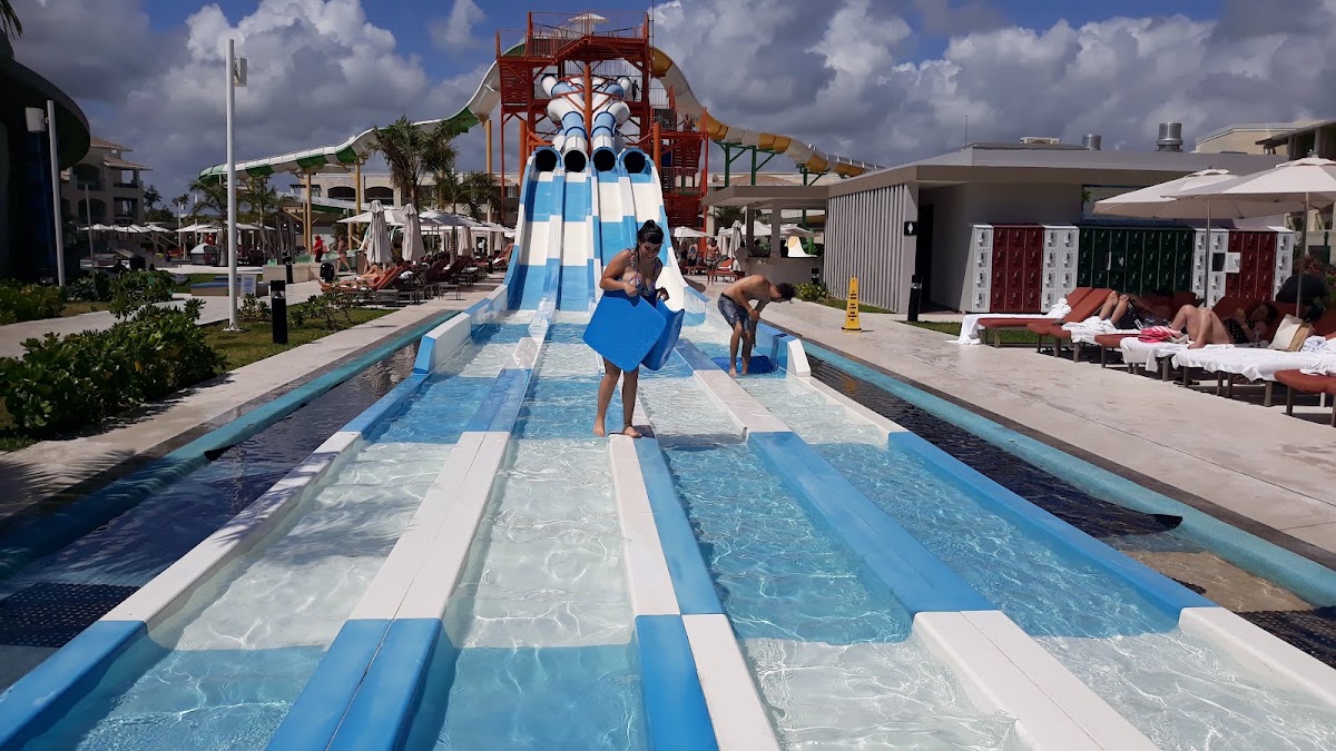 Children slide down a blue and white water slide at Moon Palace Cancun's aquatic park under cloudy skies.