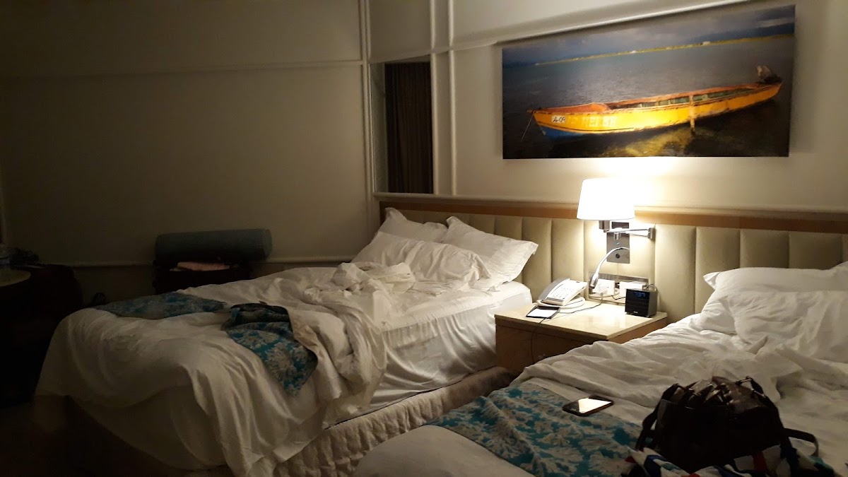 Twin beds with white linens in a resort room with a yellow boat artwork on the wall and bedside lamp.