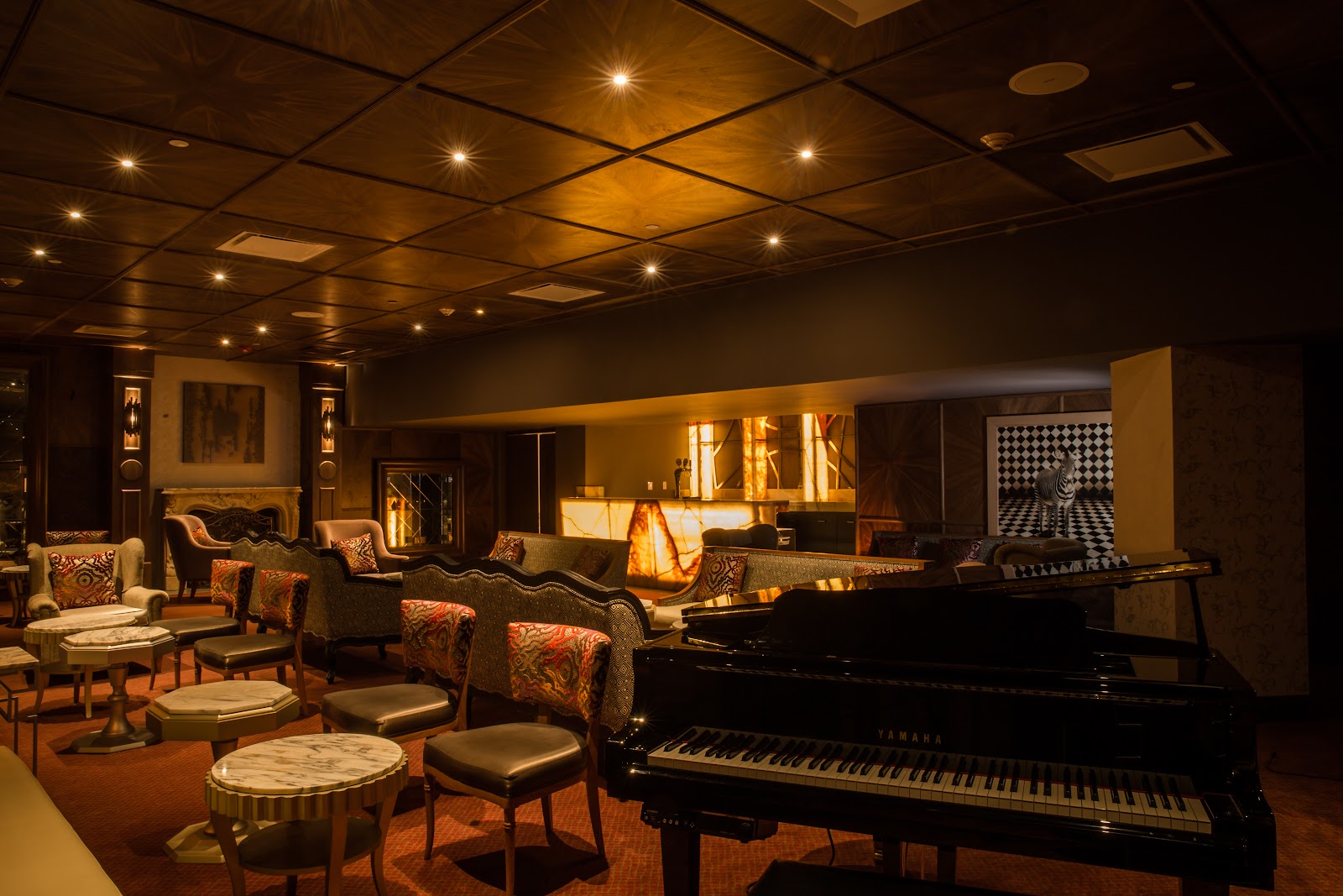 Grand piano and seating area with fireplace in warmly lit lounge at Moon Palace Jamaica.