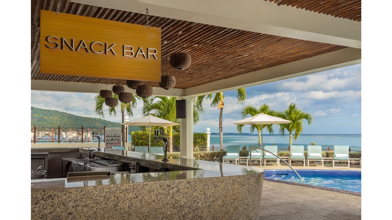 Snack bar counter with ocean view, pool, palm trees, and beach lounge chairs beyond at Moon Palace Jamaica.