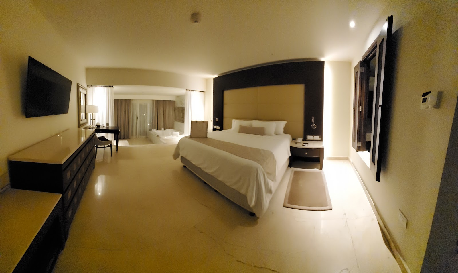 Spacious resort bedroom with two queen beds, black accent wall, flat-screen TV, and cream tile flooring throughout.