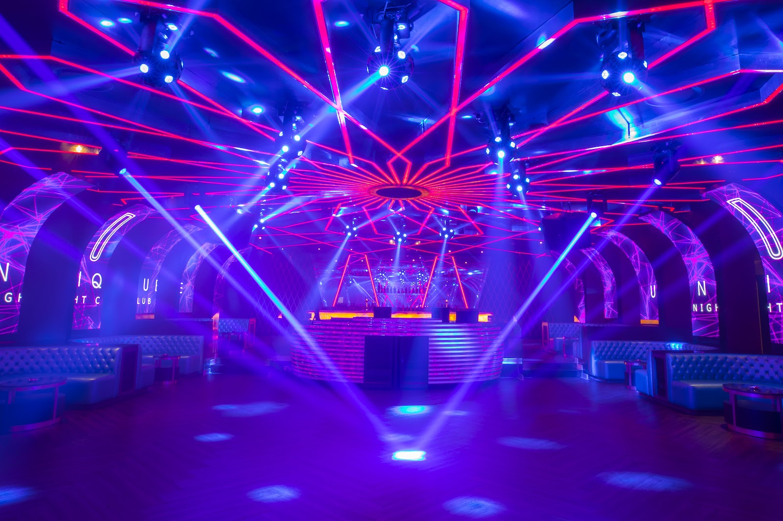 Neon nightclub interior at Moon Palace The Grand with pink and blue laser lights, DJ booth, and banquette seating.