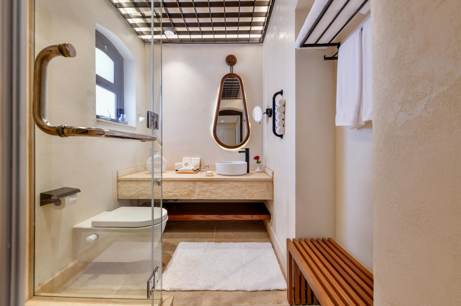 Modern bathroom with glass shower enclosure, wooden vanity with round sink, teardrop mirror, and white towels on rack.