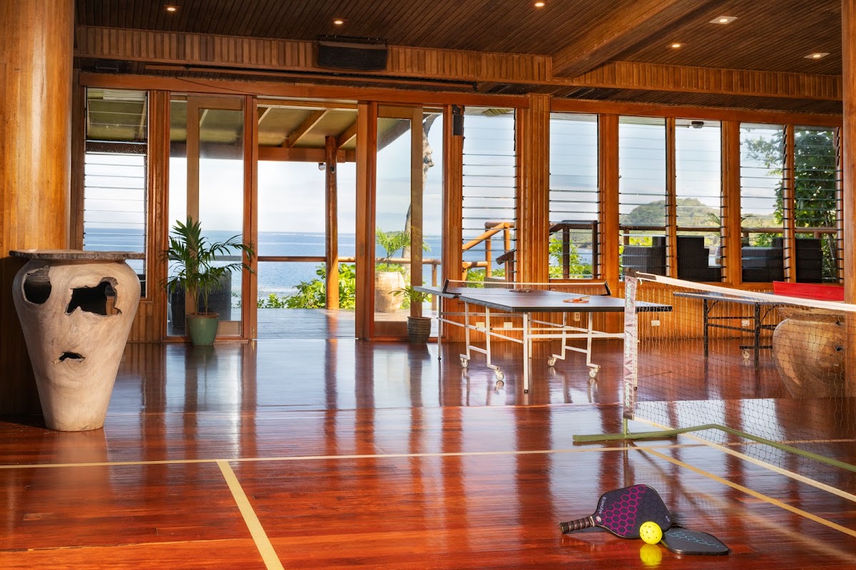 Indoor sports court with wooden floors, paddle and ball in foreground, ocean view through floor-to-ceiling windows at Namale Resort & Spa.