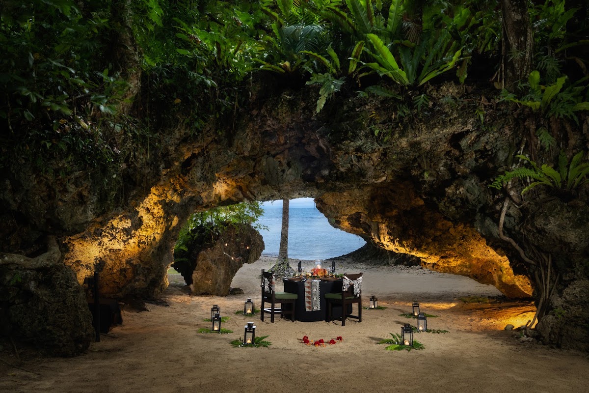 Beachside cave dining setup at Namale Resort & Spa with candlelit table framed by dramatic limestone rock formations and ocean view.