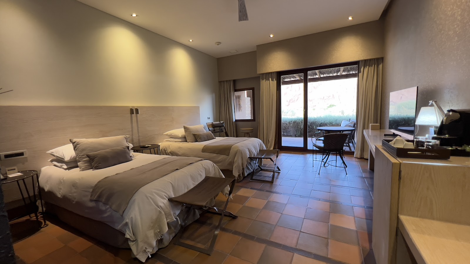 Spacious resort room with two queen beds, terracotta tile flooring, and glass doors opening to a desert landscape view at Nayara Alto Atacama.