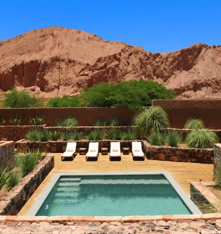 Small pool with white lounge chairs on wooden deck, surrounded by stone walls and desert landscape at Nayara Alto Atacama.