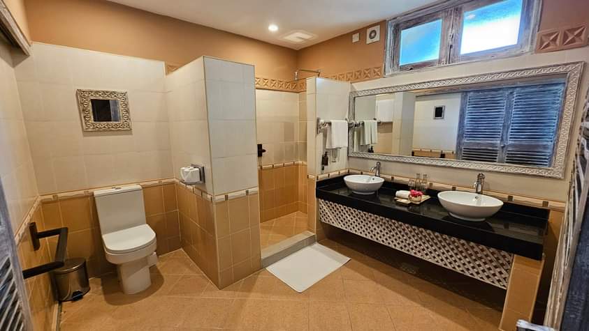 Spacious bathroom at Neptune Beach Resort with dual sinks, walk-in shower, and separate toilet area in warm earth tones.