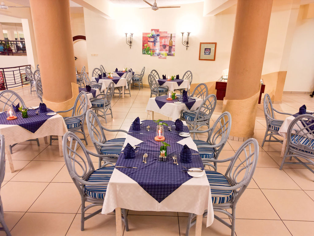 Dining room at Neptune Beach Resort with white-clothed tables topped with navy linens, striped chairs, and tall peach columns throughout the space.