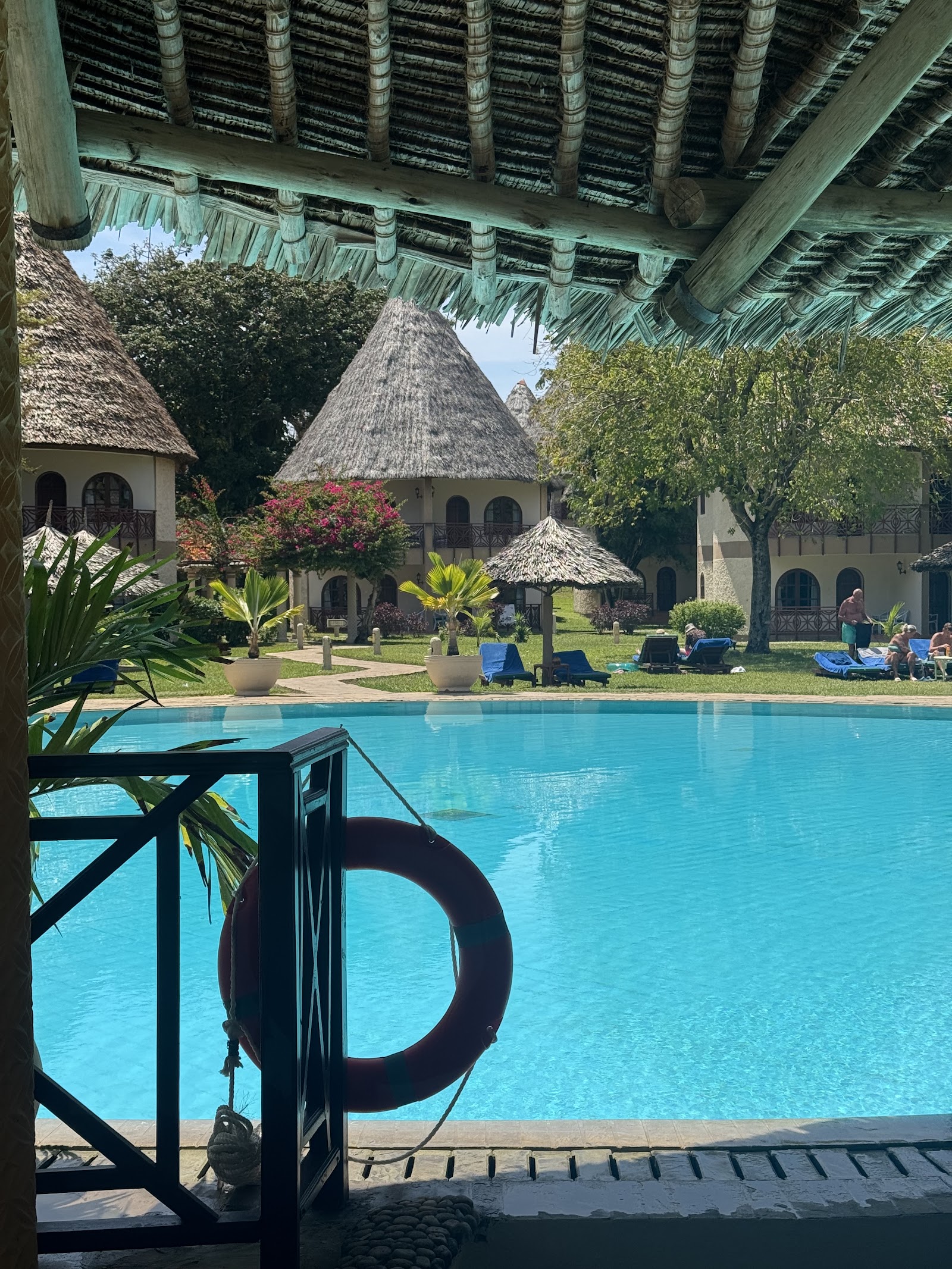 Palm-lined lawn with white lounge chairs and thatched-roof structures at Neptune Paradise Beach Resort & Spa under blue sky.