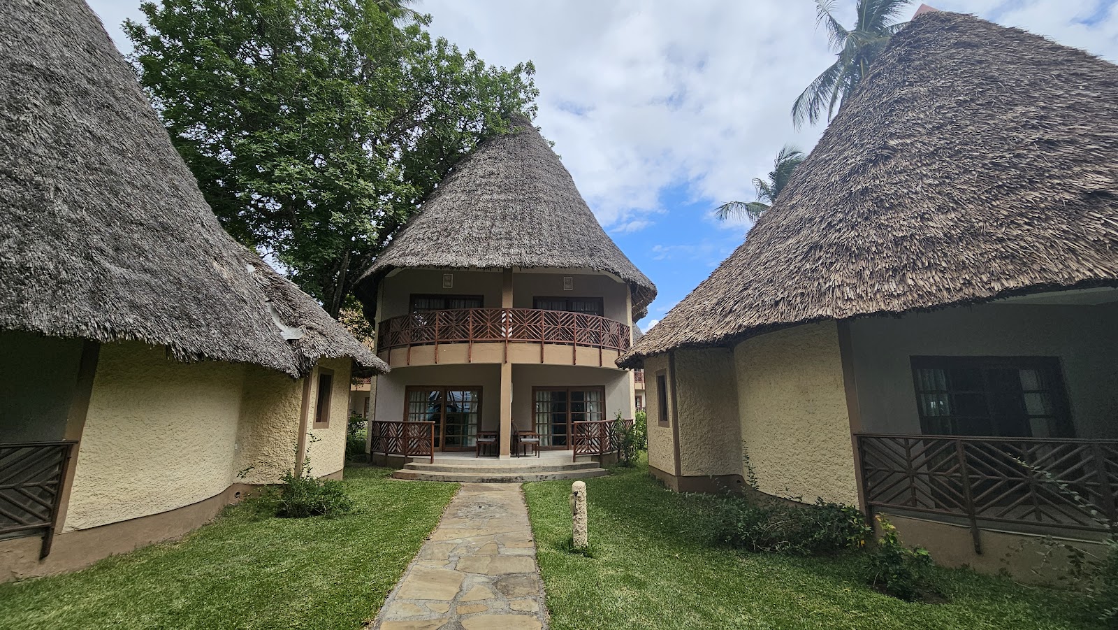 Stone pathway leading to a circular thatched-roof bungalow flanked by matching guest structures at Neptune Paradise Beach Resort & Spa.
