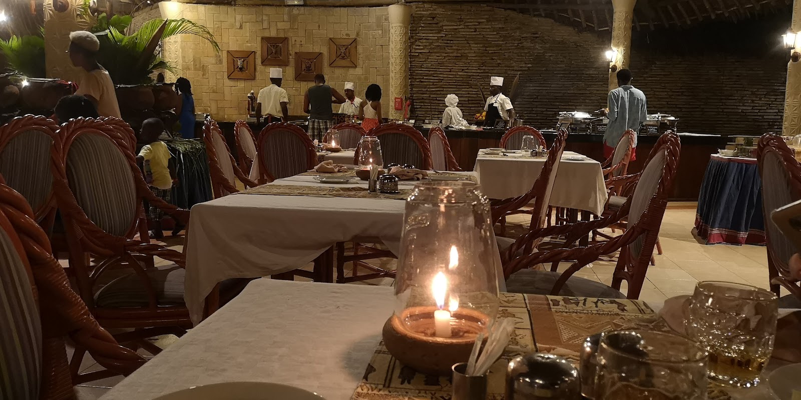 Dining room at Neptune Village Beach Resort & Spa with candlelit tables, burgundy chairs, and staff preparing the buffet along stone walls.