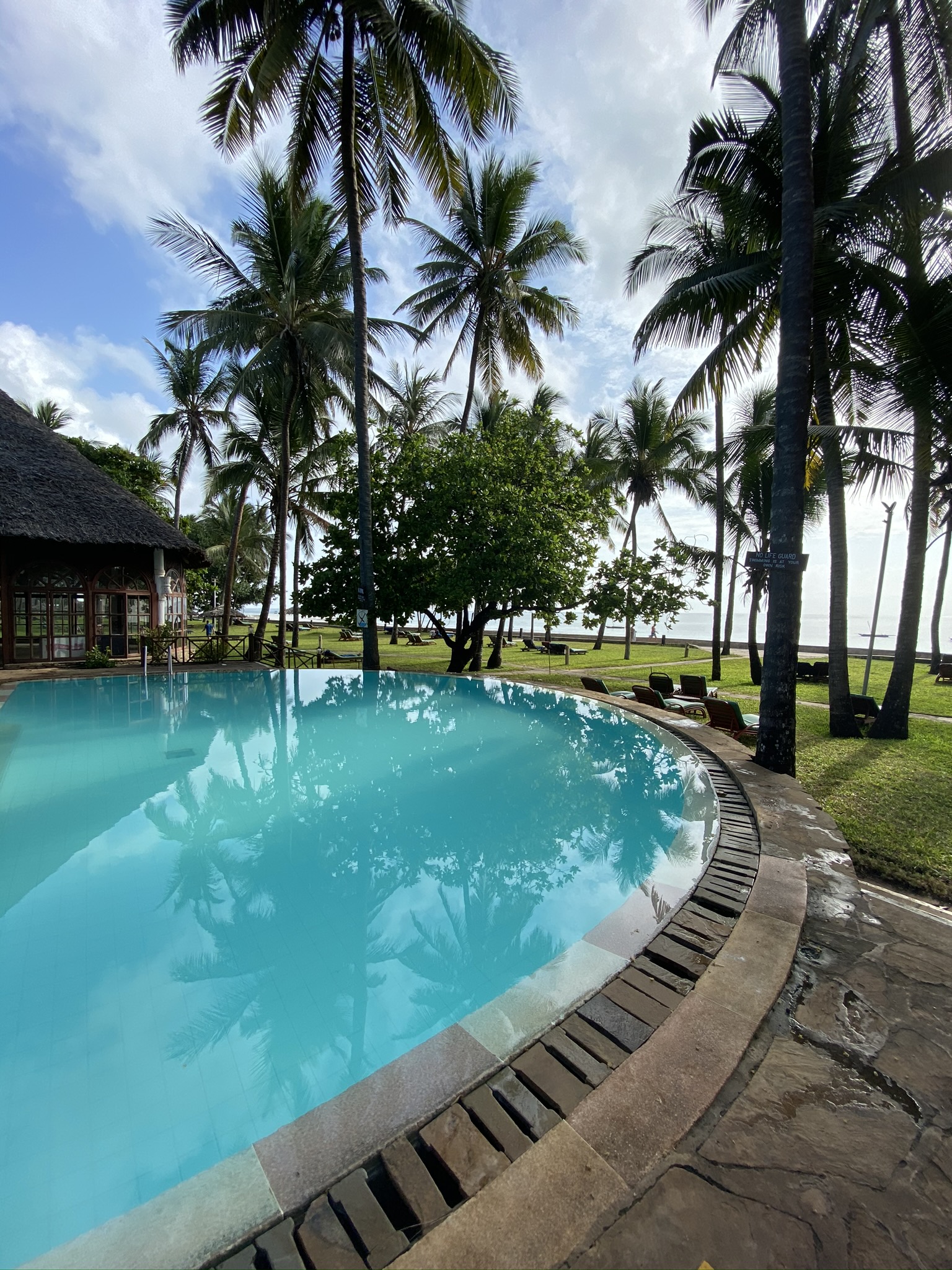 Turquoise pool with thatched-roof pavilions and palm trees at Neptune Village Beach Resort & Spa in Kenya.