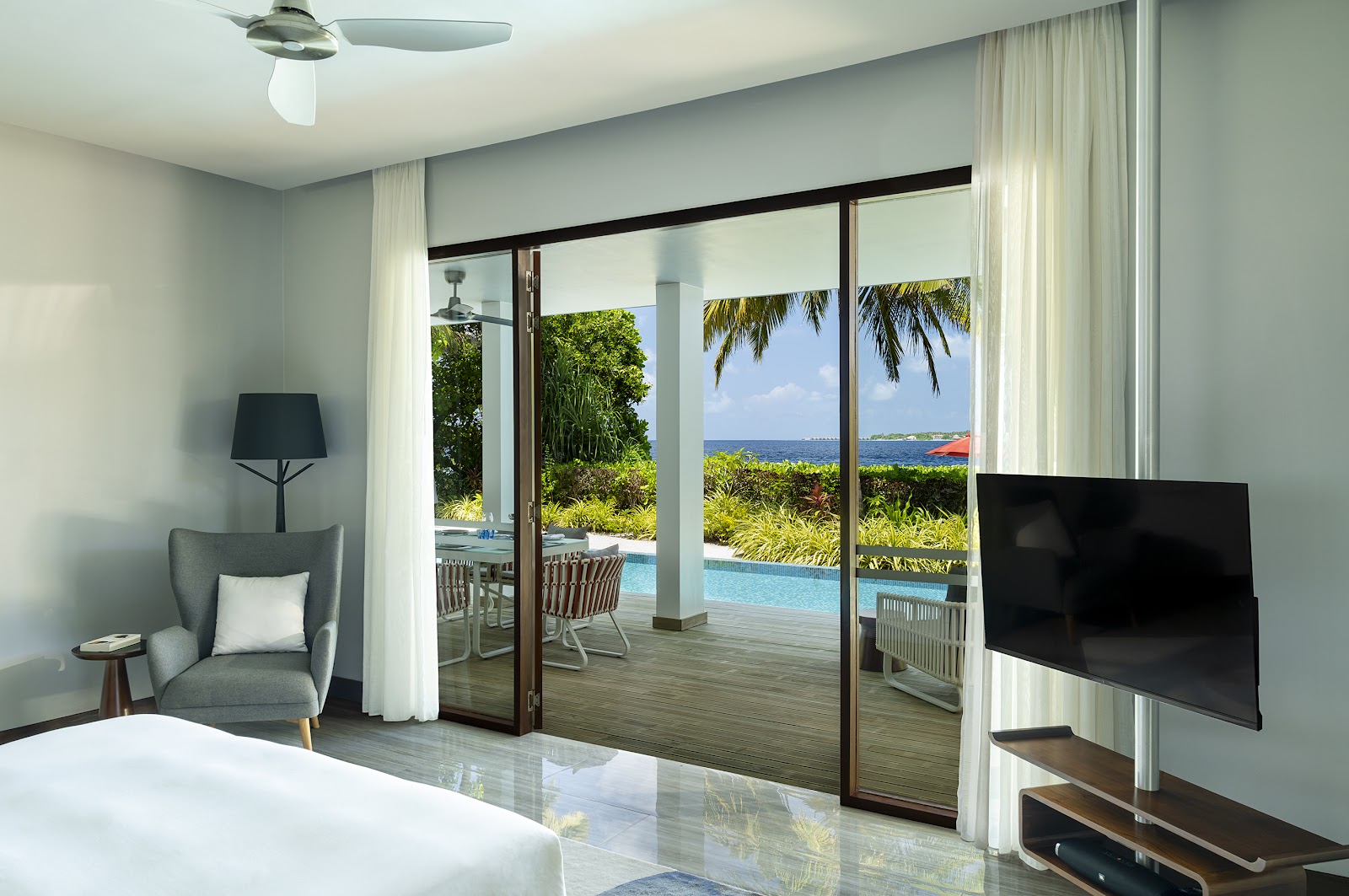 Resort room with sliding glass doors opening to a pool deck overlooking the ocean and palm trees at NIVA Dhigali Maldives.