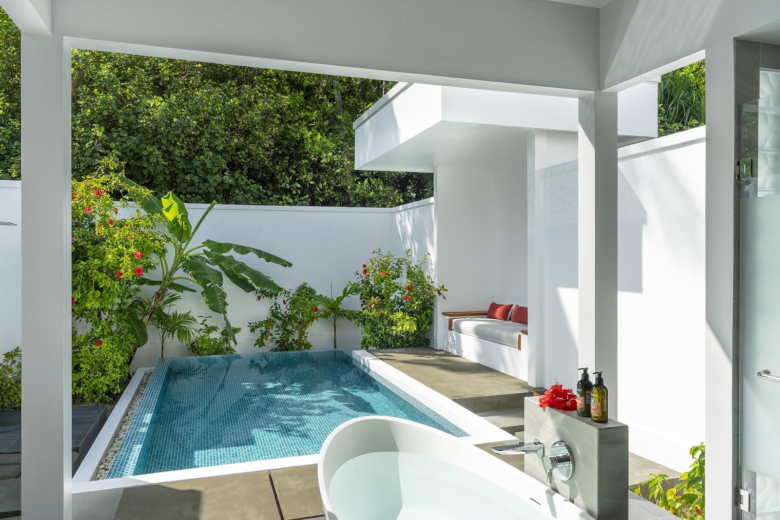 Private villa courtyard with turquoise plunge pool, white architectural features, lush green vertical gardens, soaking tub, and lounge seating at NIVA Dhigali Maldives.