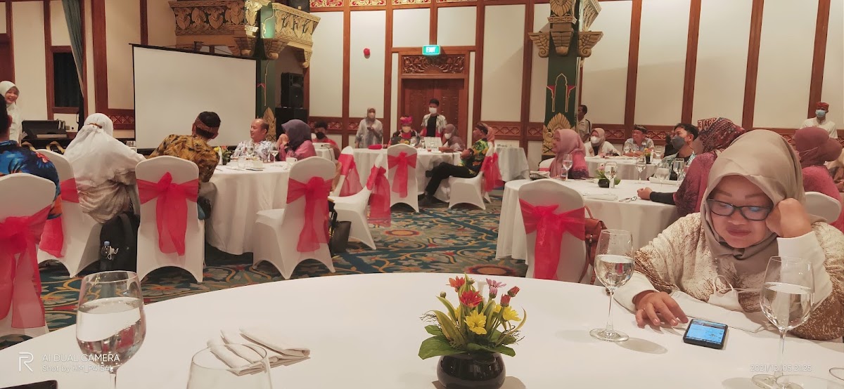 Formal banquet hall with white-clothed tables decorated with pink chair sashes, place settings, and a central floral arrangement, guests seated throughout the ornate room with red and gold architectural details.