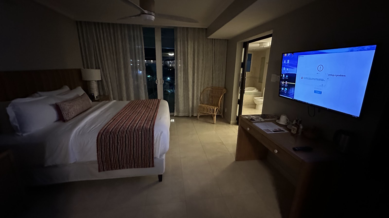 Resort bedroom with queen bed, flat-screen TV, wicker chair, and nighttime ocean view from balcony at O2 Beach Club & Spa.