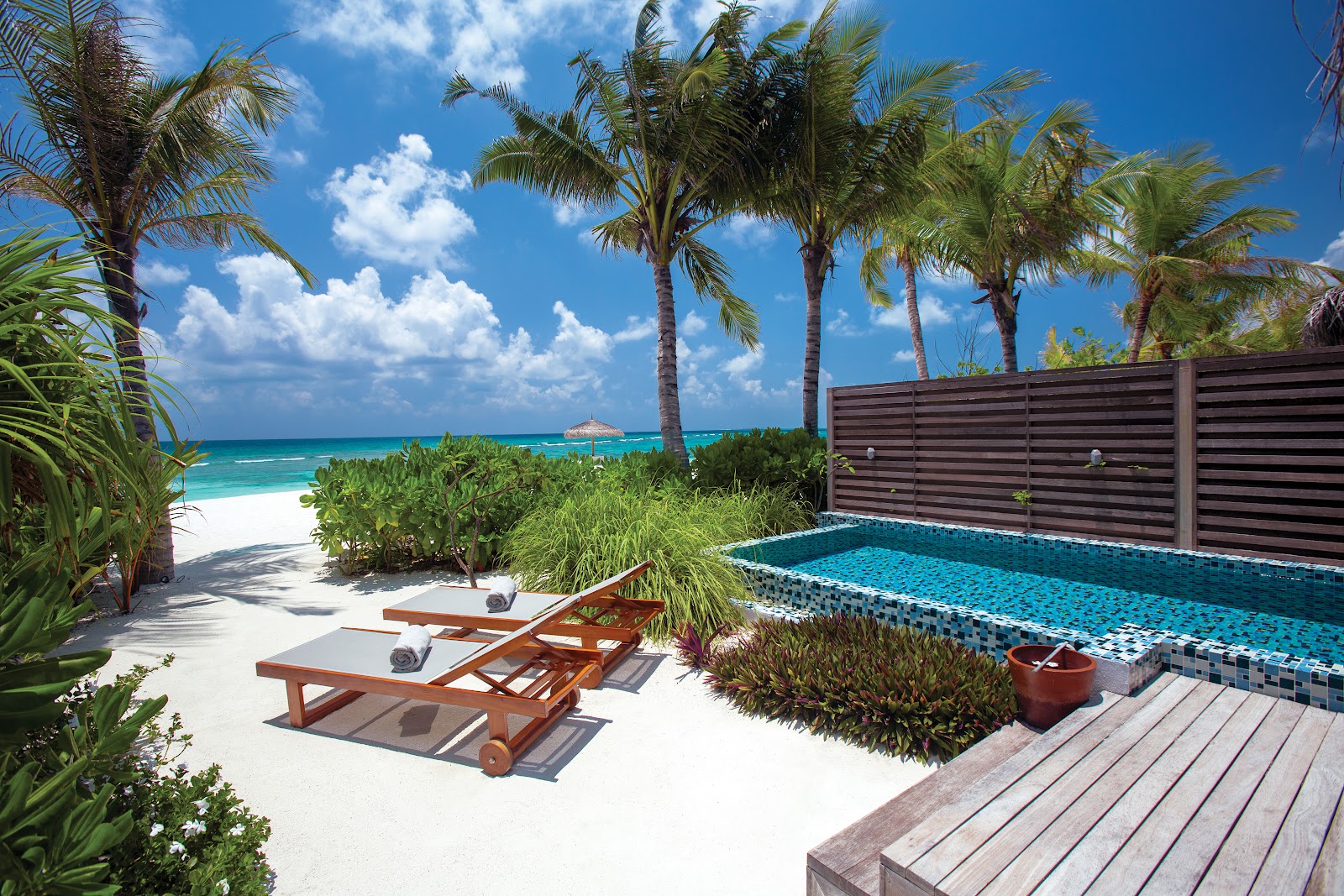 Palm-lined beach with wooden lounge chairs, private pool, and turquoise ocean at OBLU SELECT Sangeli under blue sky.
