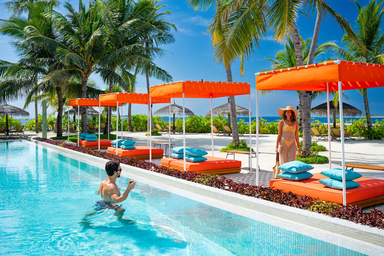 Guest swimming in turquoise pool at OBLU SELECT Sangeli with orange canopies, lounge chairs, and ocean view beyond palm trees.