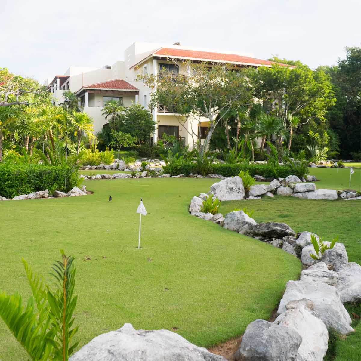 Resort golf course with stone features and tropical vegetation bordering manicured lawn, white buildings with terracotta roofs visible beyond.