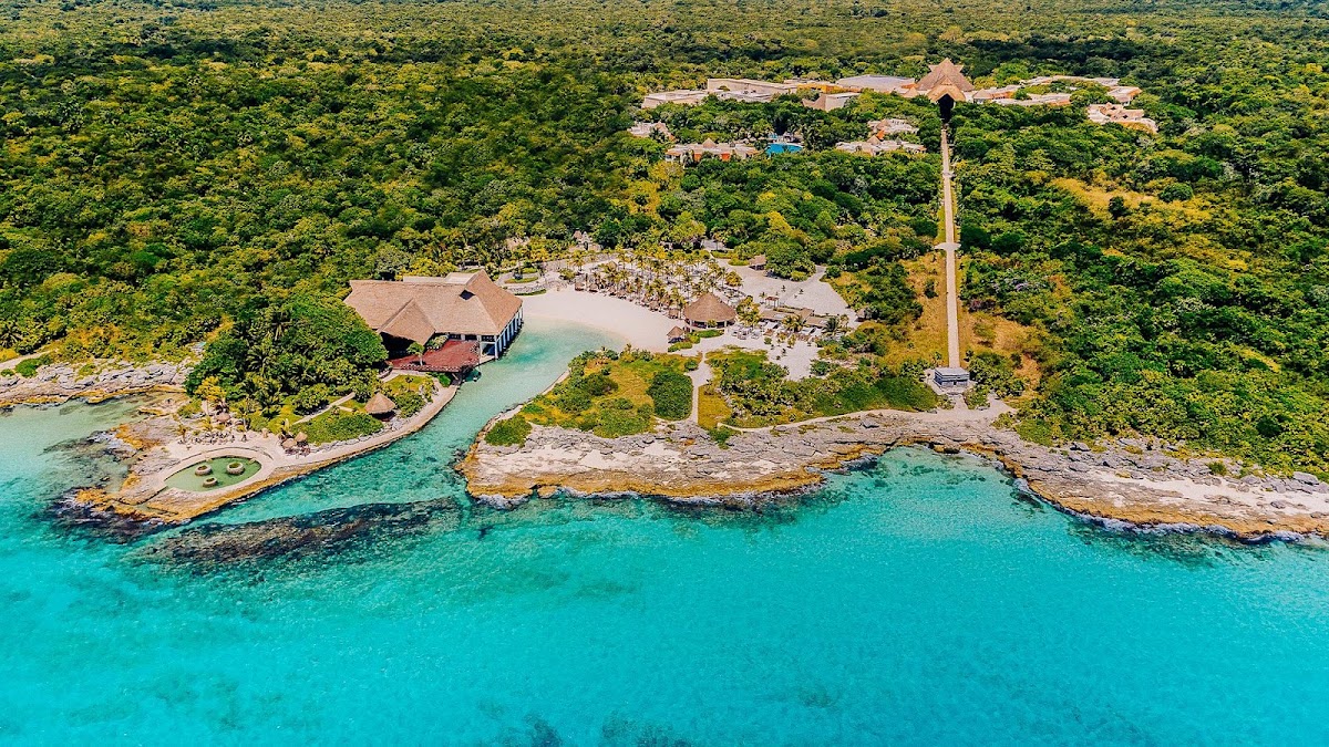 Aerial view of Occidental at Xcaret Destination nestled between turquoise Caribbean waters and dense jungle, with beach, lagoon, and main lodge visible.