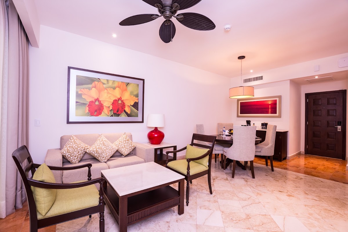 Living room with pink ceiling, beige sofa, yellow accent chairs, ceiling fan, and flower artwork on walls.