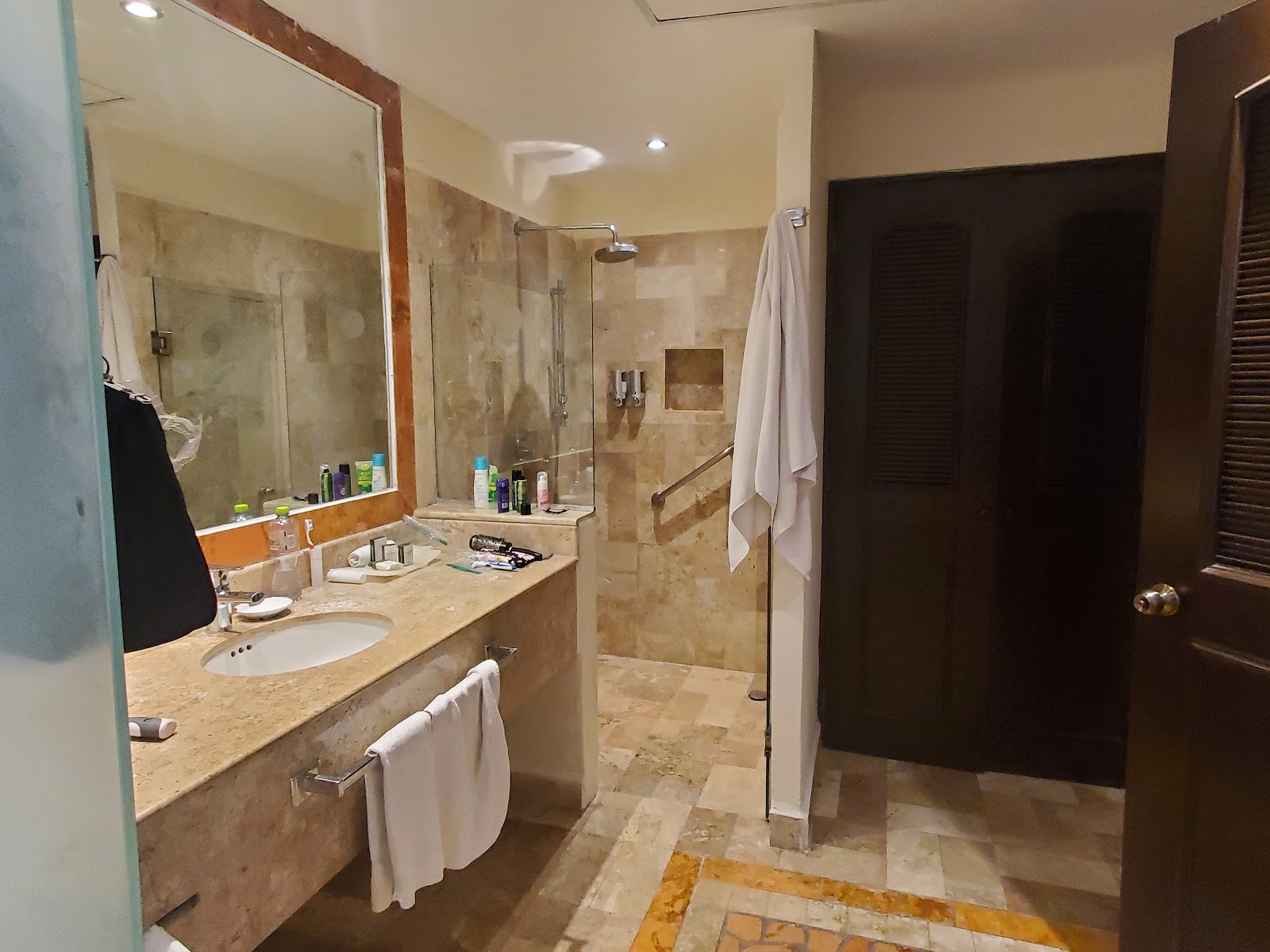 Bathroom with marble countertop, large mirror, walk-in shower with glass enclosure, and white towels draped over rack.