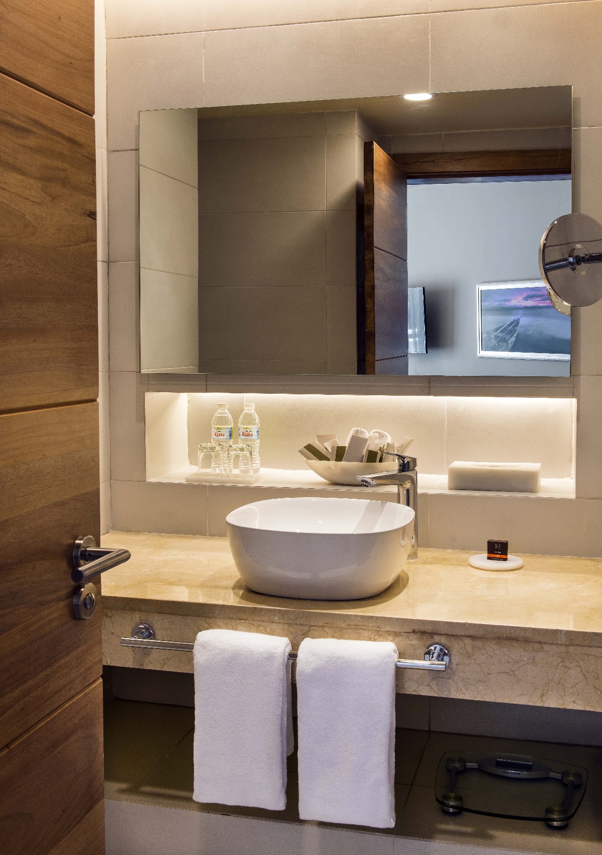 Modern bathroom with white vessel sink, illuminated mirror, complimentary toiletries, and white towels on stone countertop.