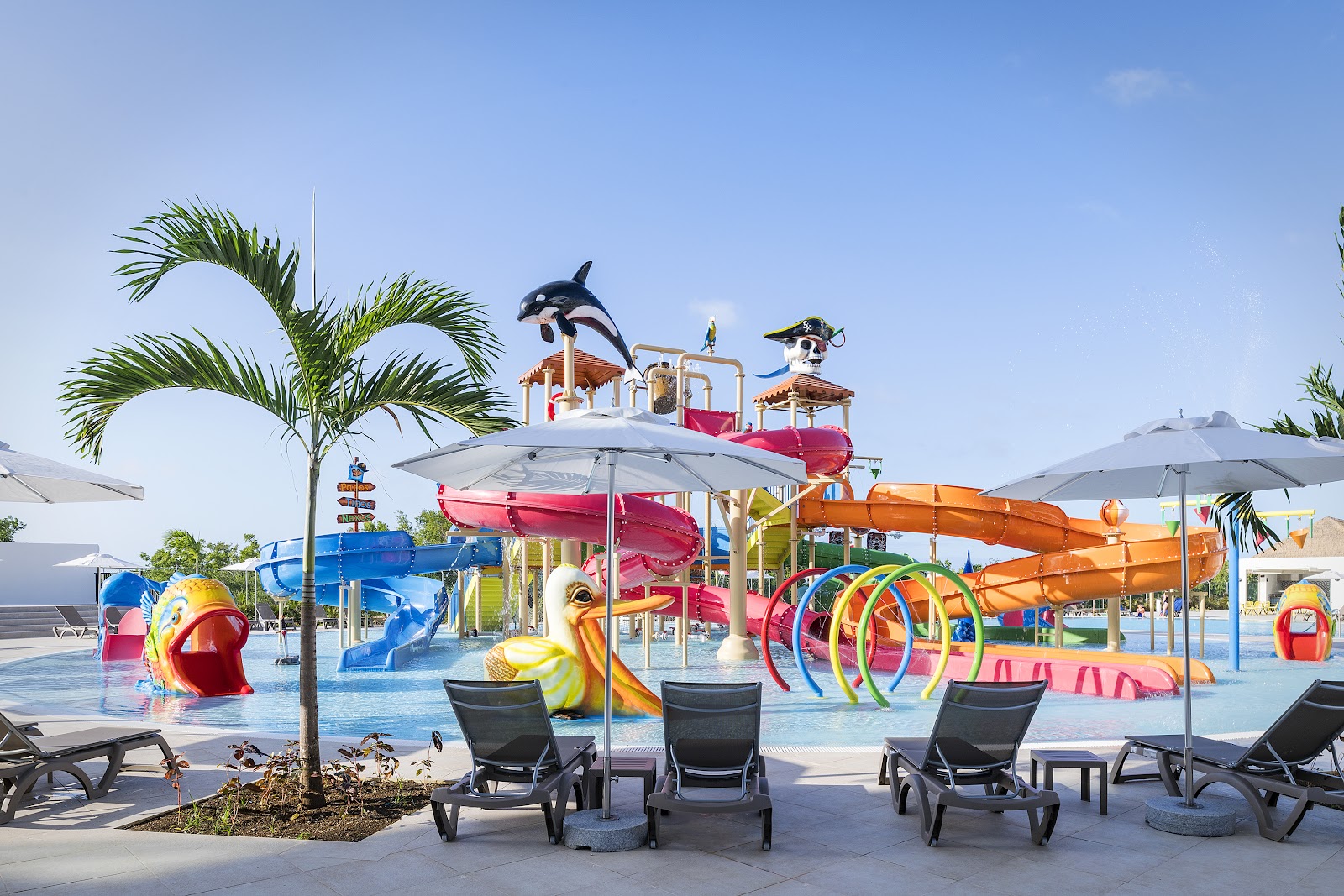 Colorful water park at Ocean Coral Spring with slides, playgrounds, and lounge chairs under umbrellas on a clear day.