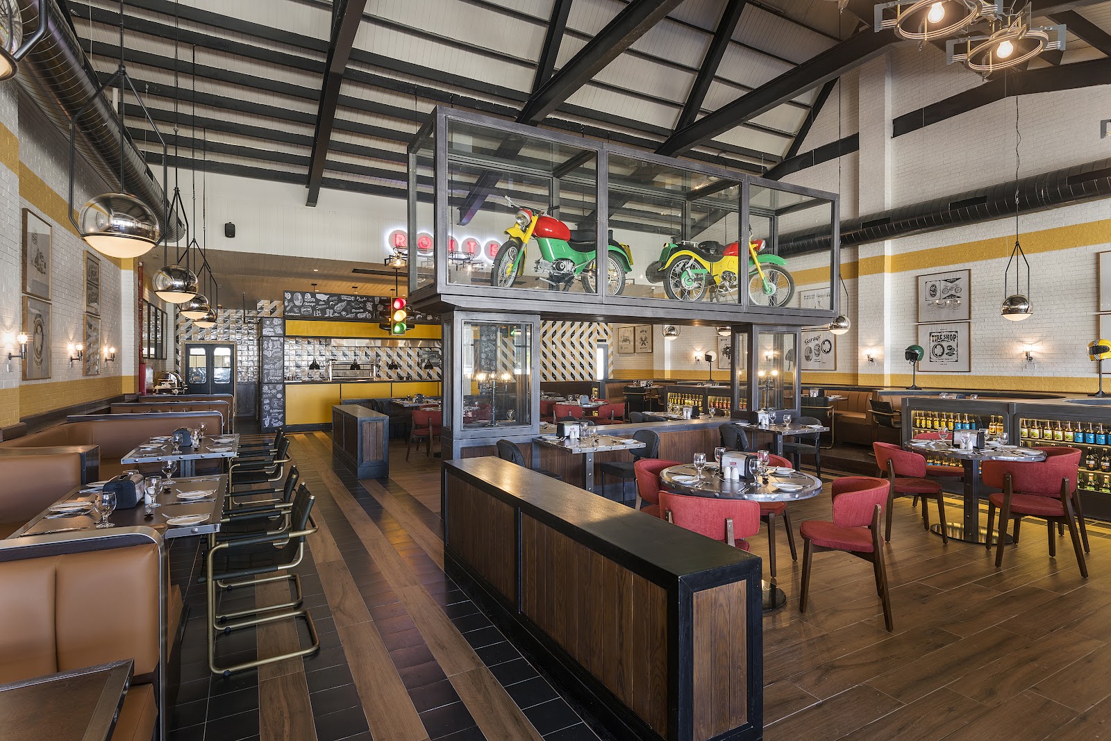 Modern dining room with colorful vintage motorcycles displayed above glass partitions, red chairs, wood tables, and yellow and white striped walls.