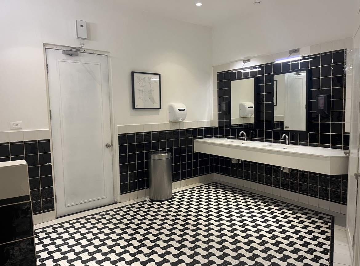 Resort bathroom with black tile walls, double sink vanity, geometric black and white floor, and shower enclosure.