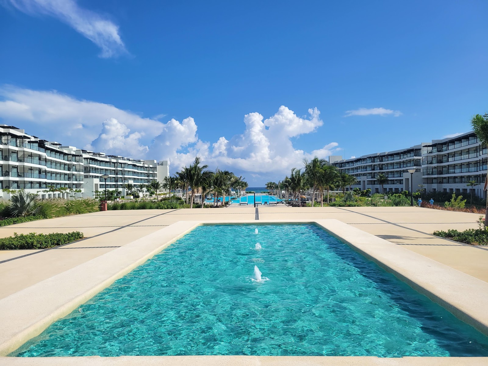 Linear pool with turquoise water flanked by sand, leading toward beachfront buildings and ocean at Ocean Eden Bay.