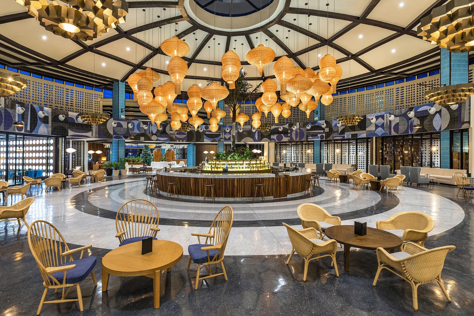 Spacious lobby with woven pendant lights, wooden chairs with blue cushions around tables, and a circular bar in the center at Ocean Riviera Paradise.