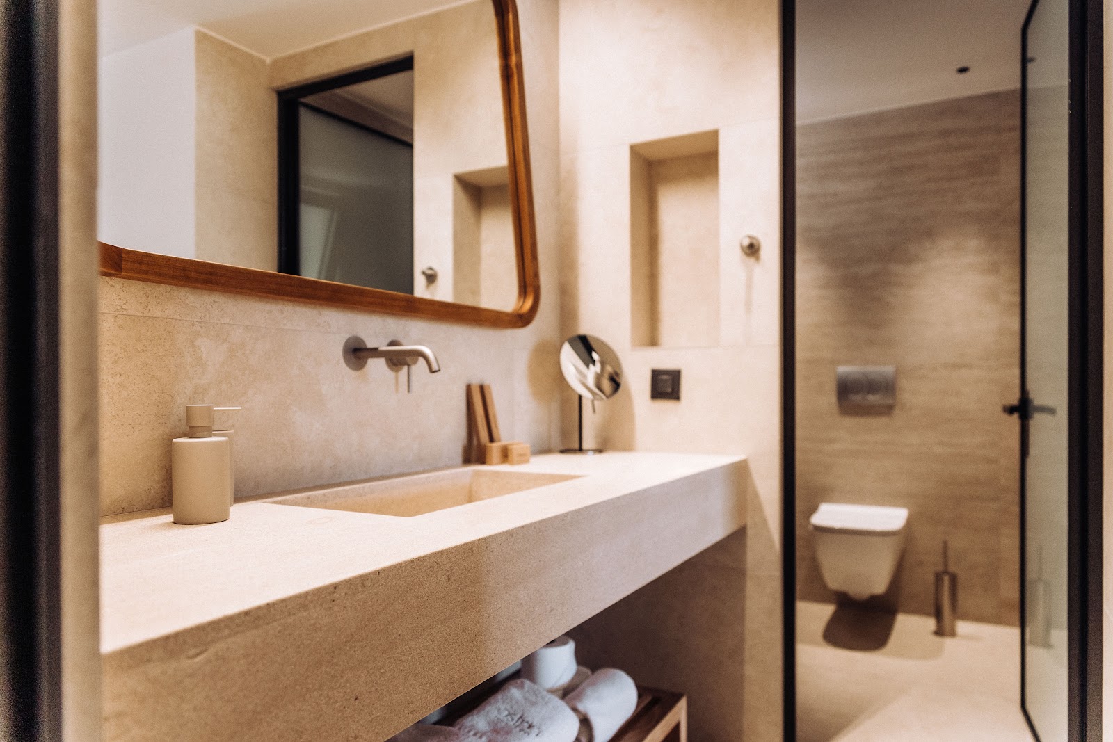 Modern bathroom with long stone vanity, wooden-framed mirror, and glass shower enclosure visible in background at Ostria Resort & Spa.