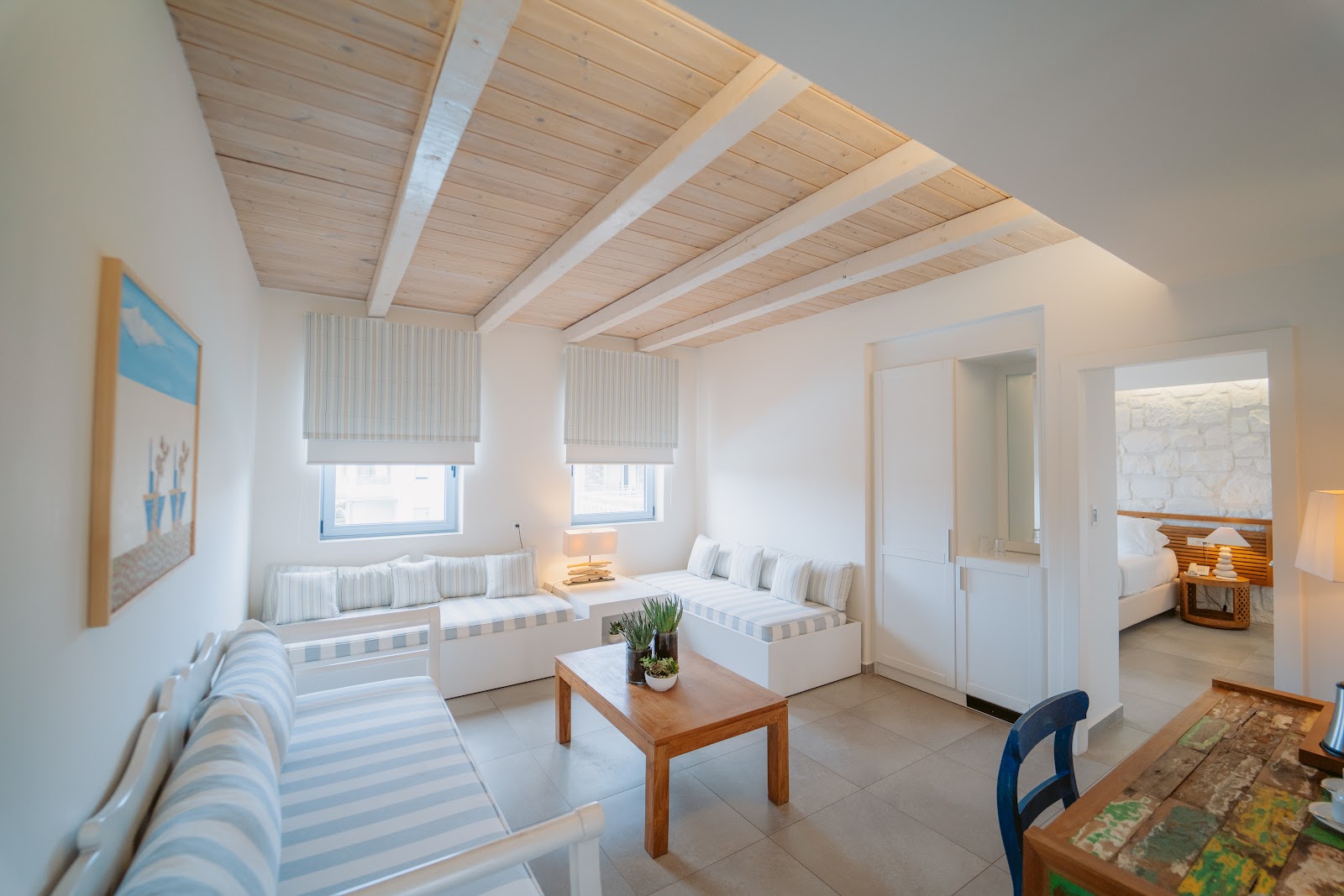 Bright suite with wooden ceiling beams, striped sofas, built-in window seating, and views into adjoining bedroom at Ostria Resort & Spa.
