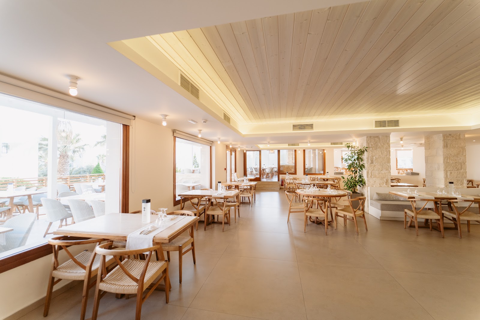 Bright dining room with wooden chairs and tables, linear ceiling, large windows overlooking terrace at Ostria Resort & Spa.