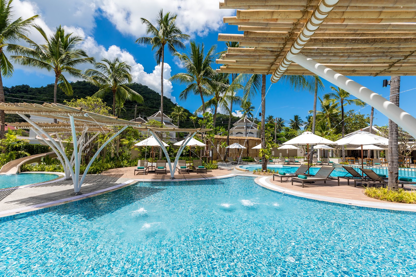 Turquoise pool with white pergolas and lounge chairs, surrounded by palm trees and white umbrellas at OUTRIGGER Koh Samui Beach Resort.