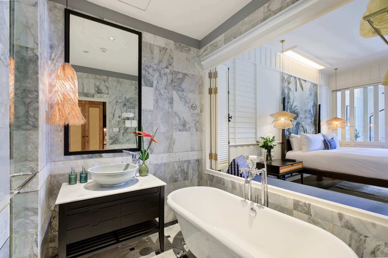 Bathroom with marble tile walls, freestanding tub, black vanity with round sink, and view into adjoining bedroom at OUTRIGGER Koh Samui Beach Resort.