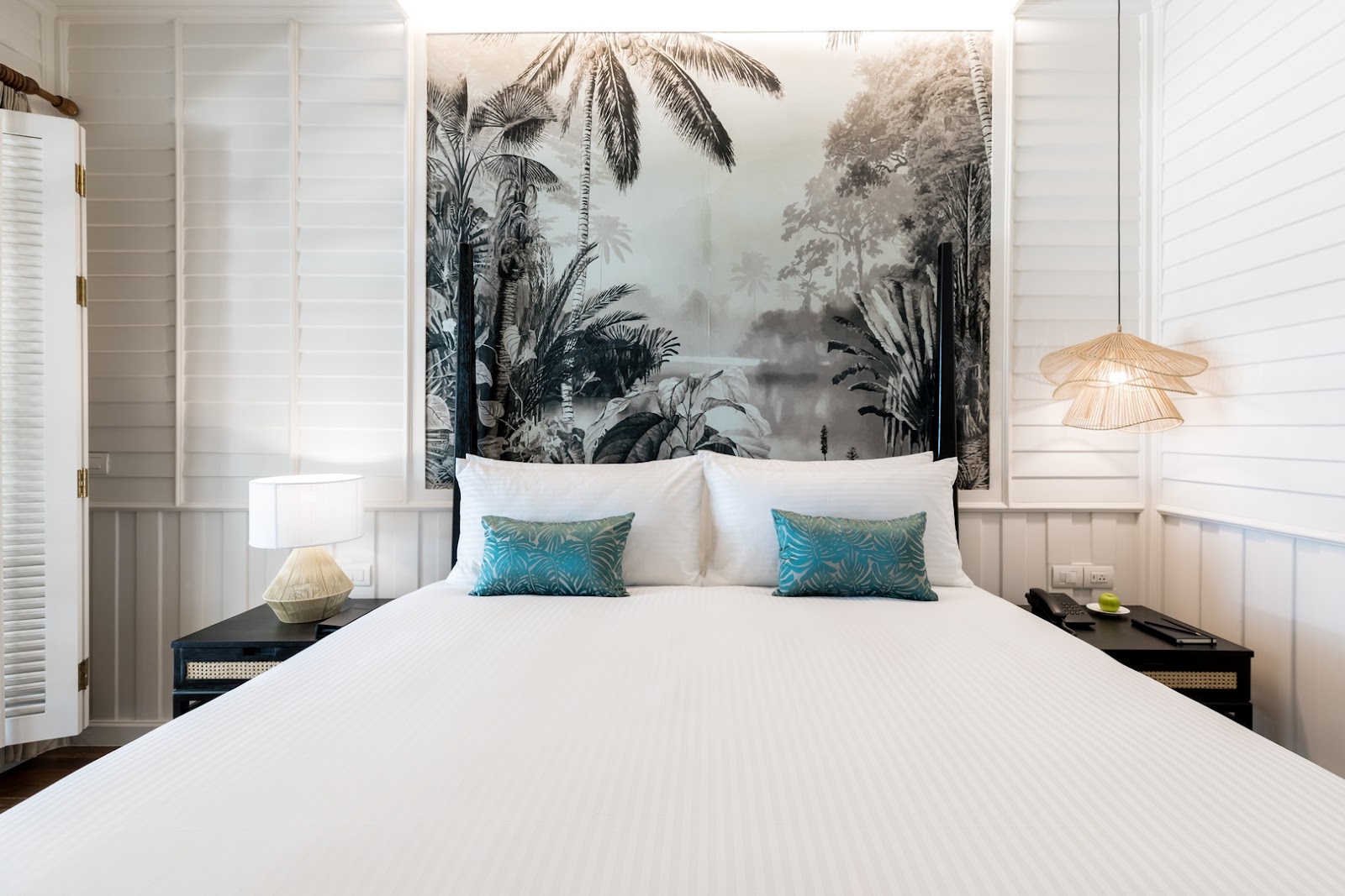 White bedroom with queen bed, blue patterned pillows, black nightstands, and large botanical artwork above headboard.