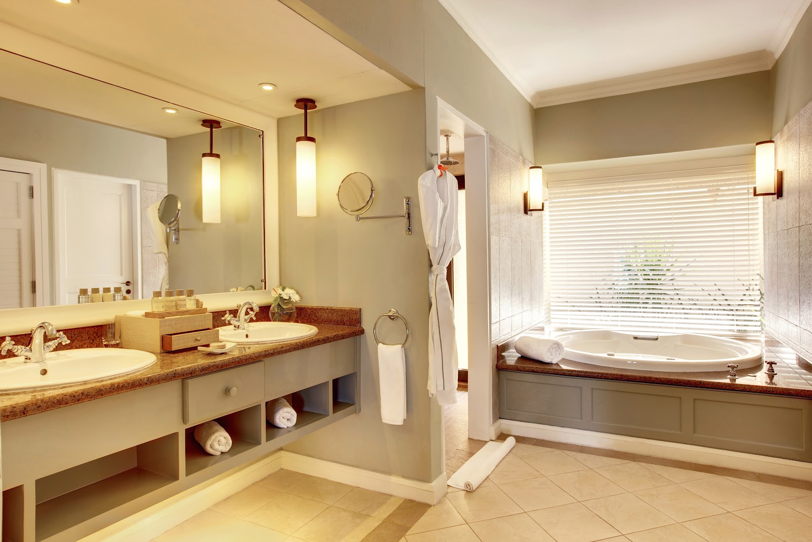Spacious bathroom with dual vanities, soaking tub by a window with shutters, and separate glass shower enclosure with pendant lighting.