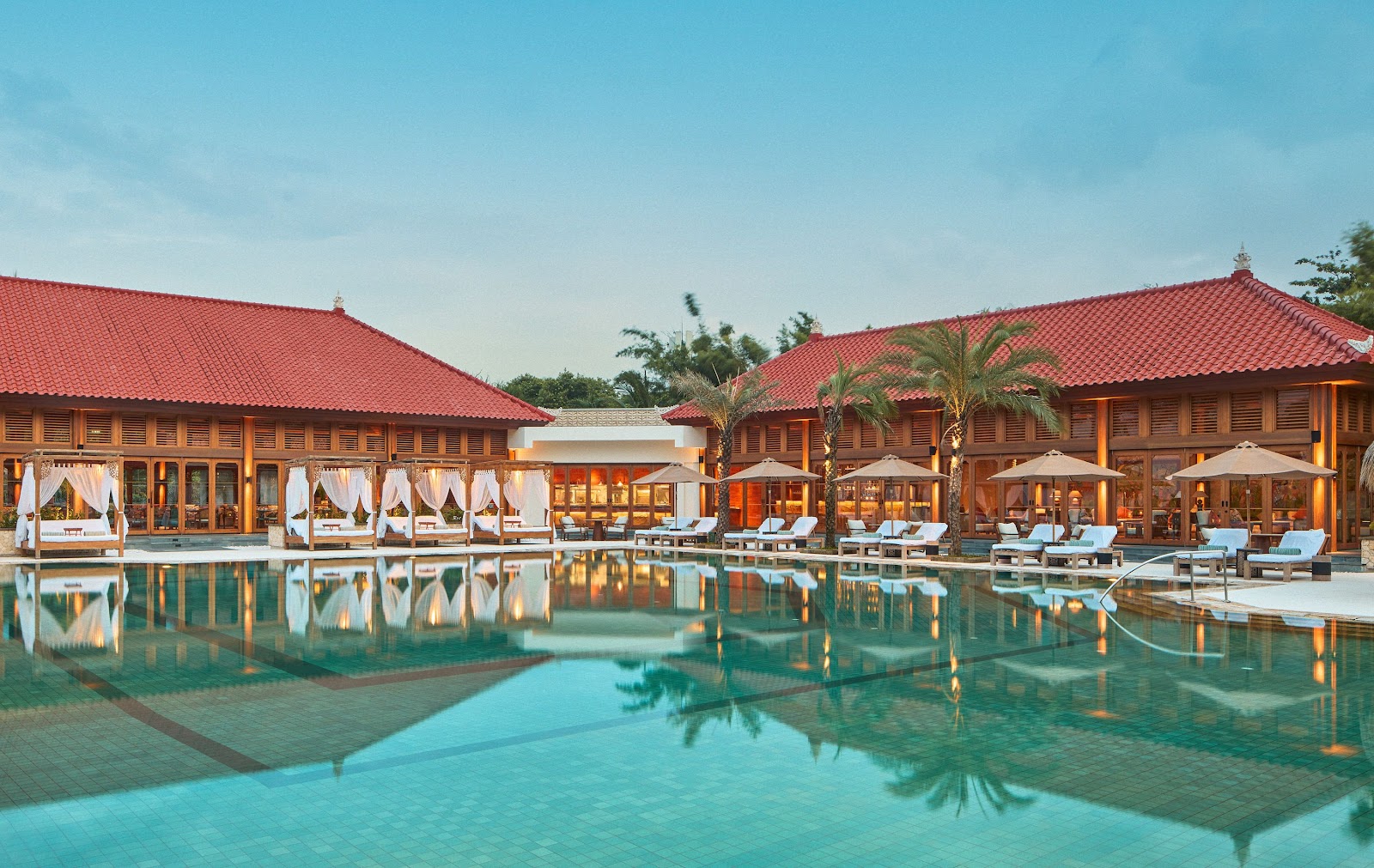 Turquoise lagoon pool at Paradisus by Meliá Bali with thatched-roof gazebo, stone walls, tropical palms, and yellow flowering plants in foreground.