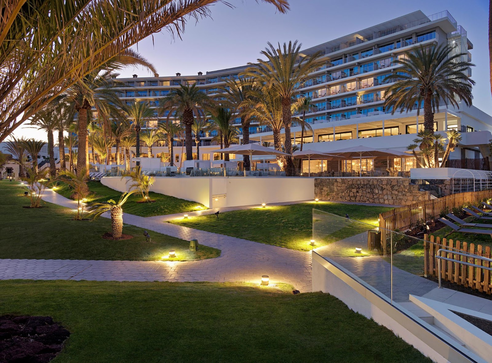 Open-concept lobby bar at Paradisus Gran Canaria with woven pendant lights, wooden seating, marble and wood flooring, and potted plants throughout.