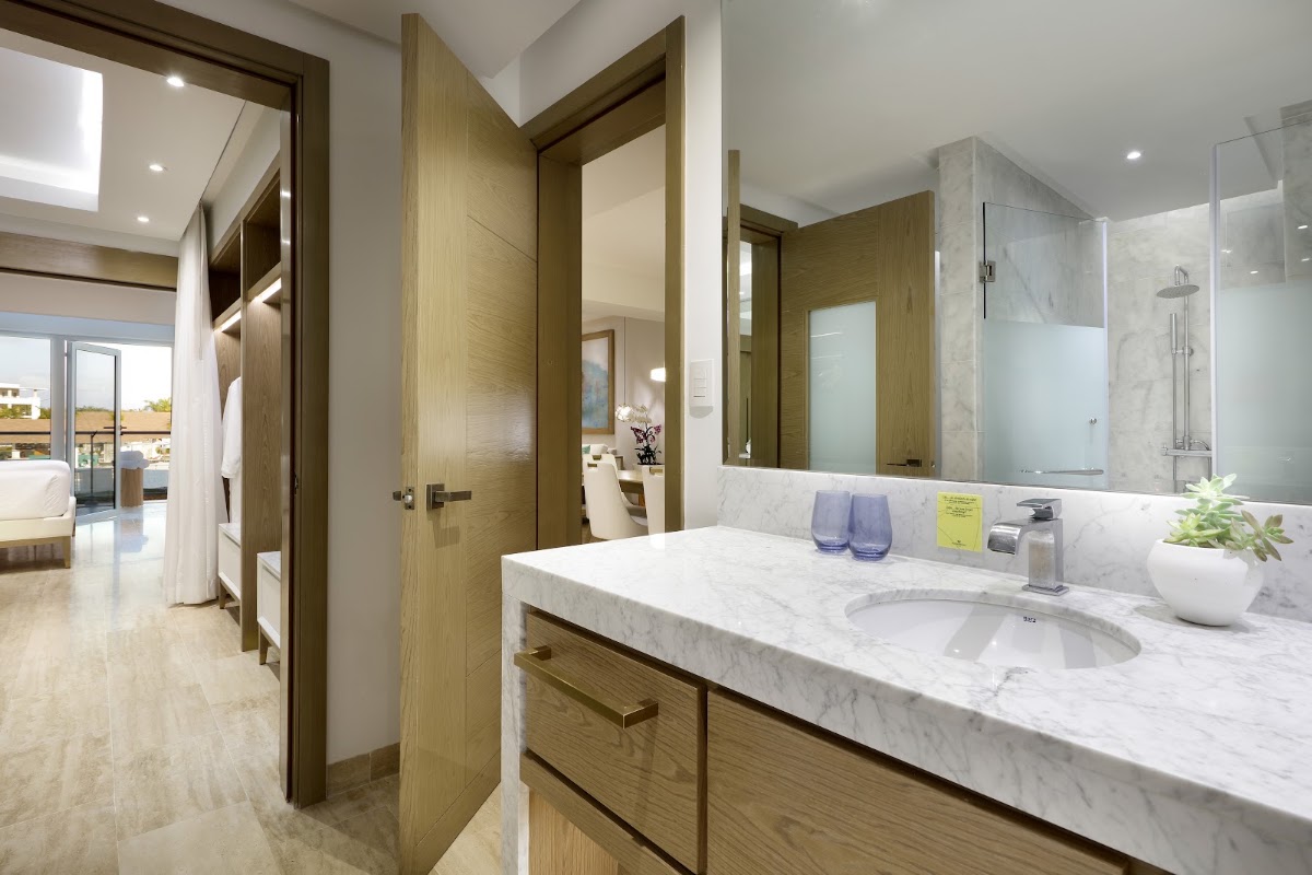 Modern bathroom with marble countertop, dual sink, wood cabinetry, and glass shower enclosure, opening to bedroom suite.
