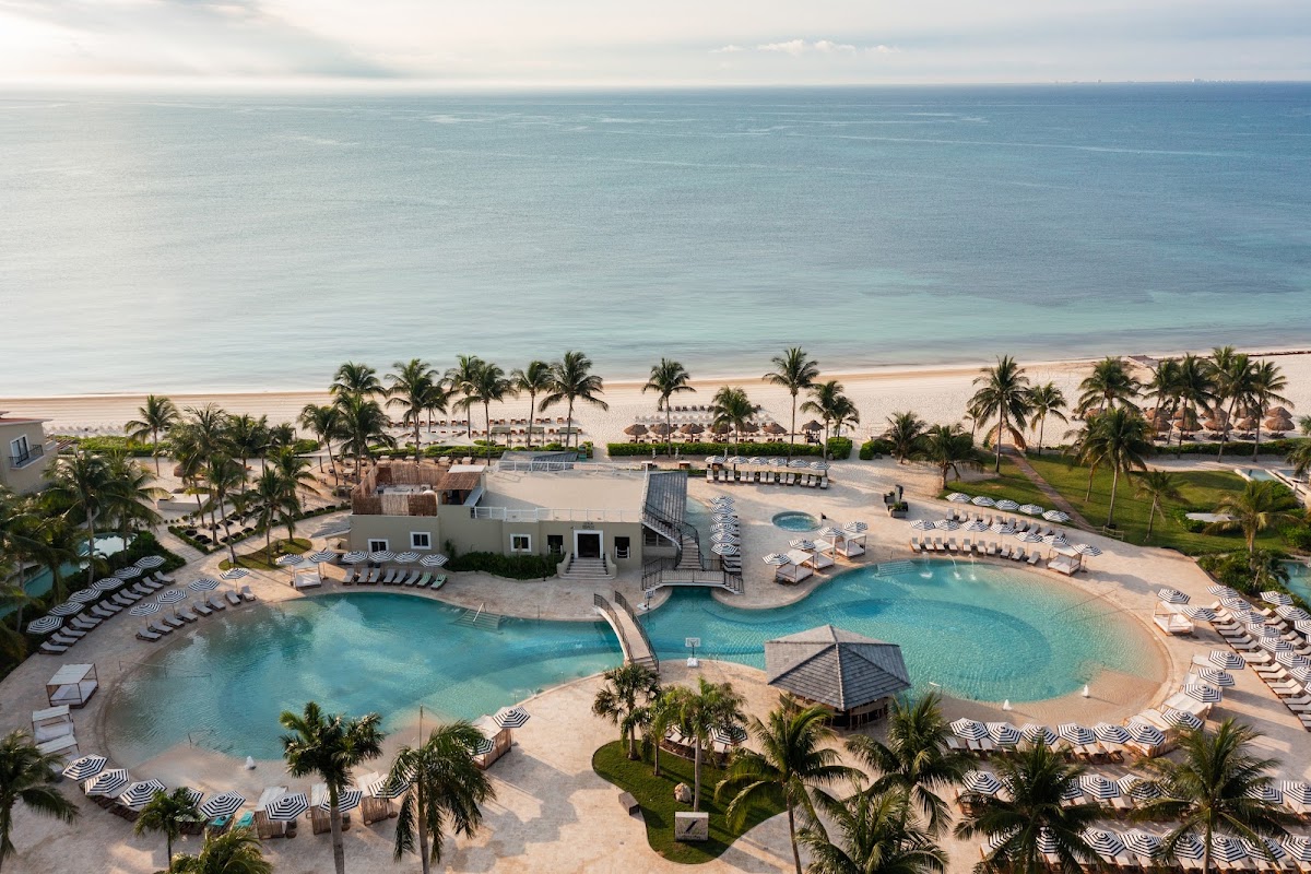 Park Hyatt Riviera Maya pool deck overlooking turquoise water, white loungers, and palm trees lining the beach.