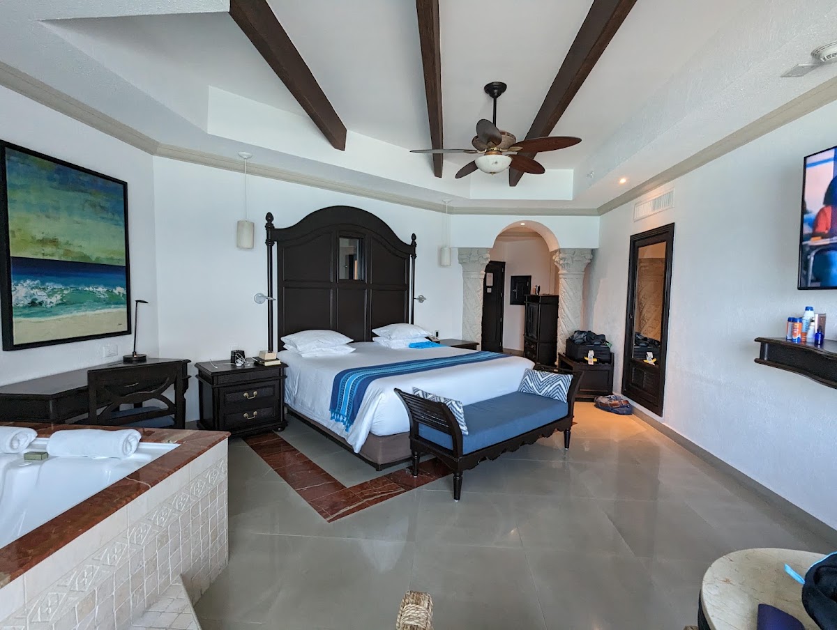 Spacious resort bedroom with black four-poster bed, white linens, ceiling fan, and beach artwork on walls.
