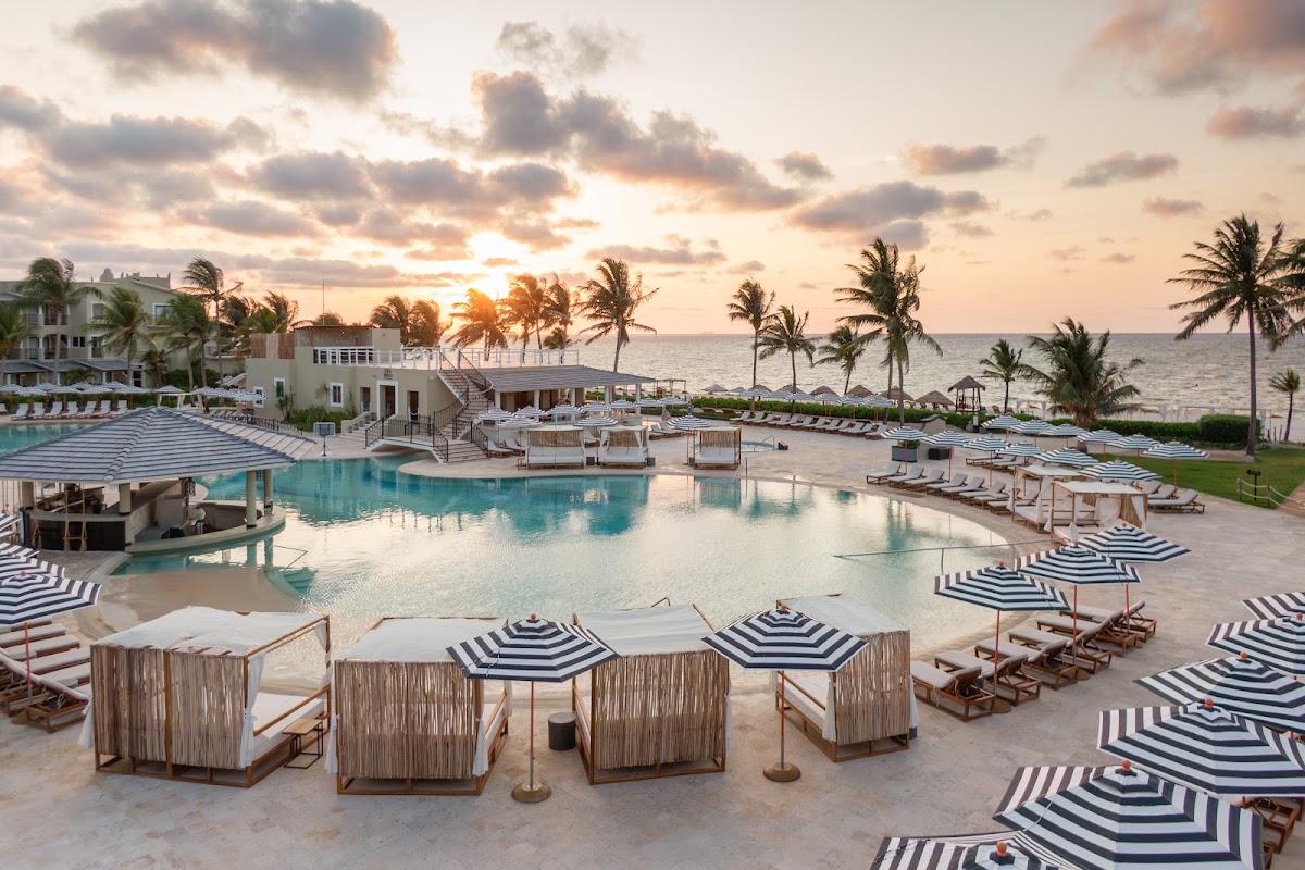 Park Hyatt Riviera Maya pool and beach at sunset with striped umbrellas, lounge chairs, and palm trees lining the ocean.
