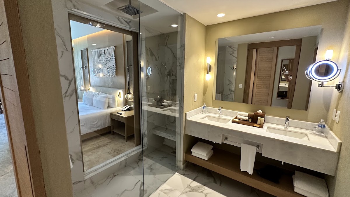 Spacious bathroom with marble shower enclosure, dual vanity sinks, and view of bedroom beyond in Park Hyatt Riviera Maya suite.