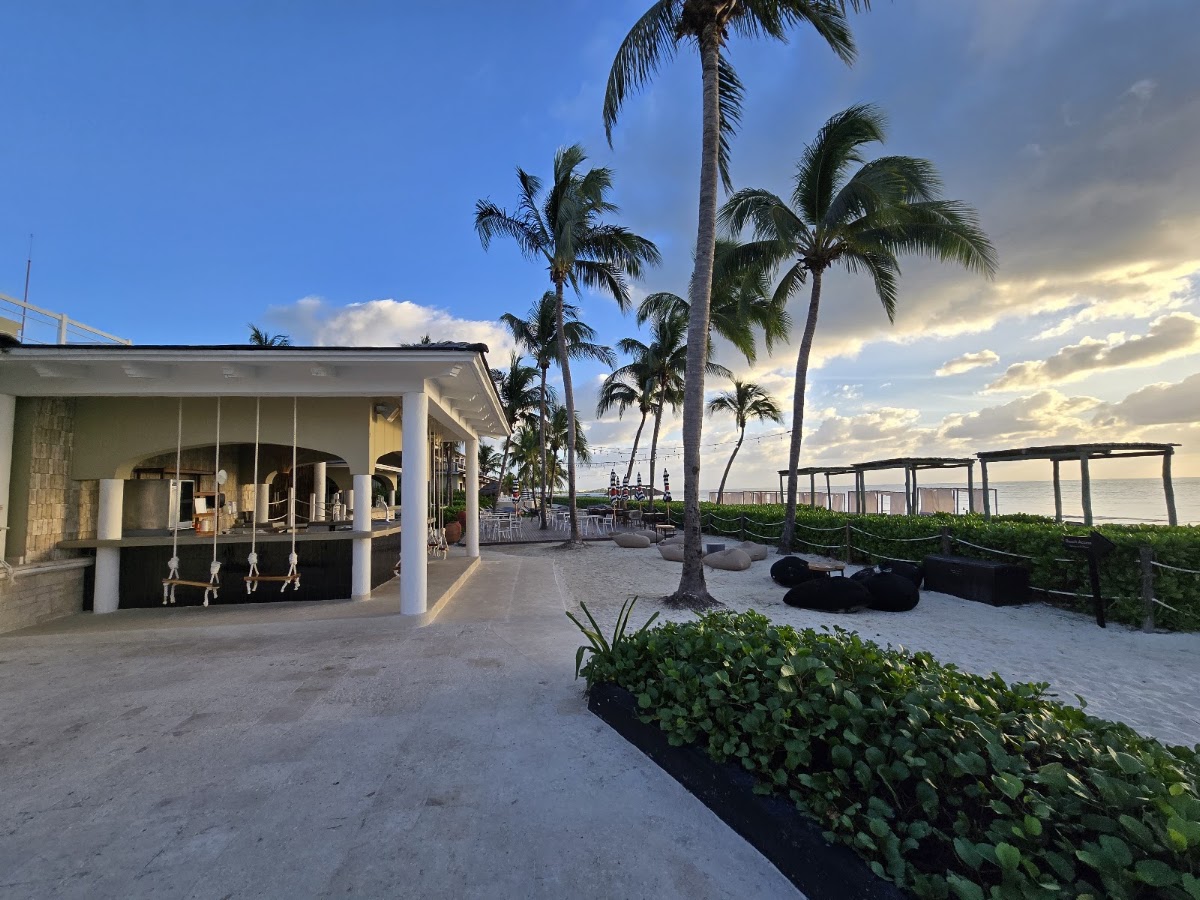 Beachfront bar and lounge area at Park Hyatt Riviera Maya with palm trees, sand, and ocean view at dusk.