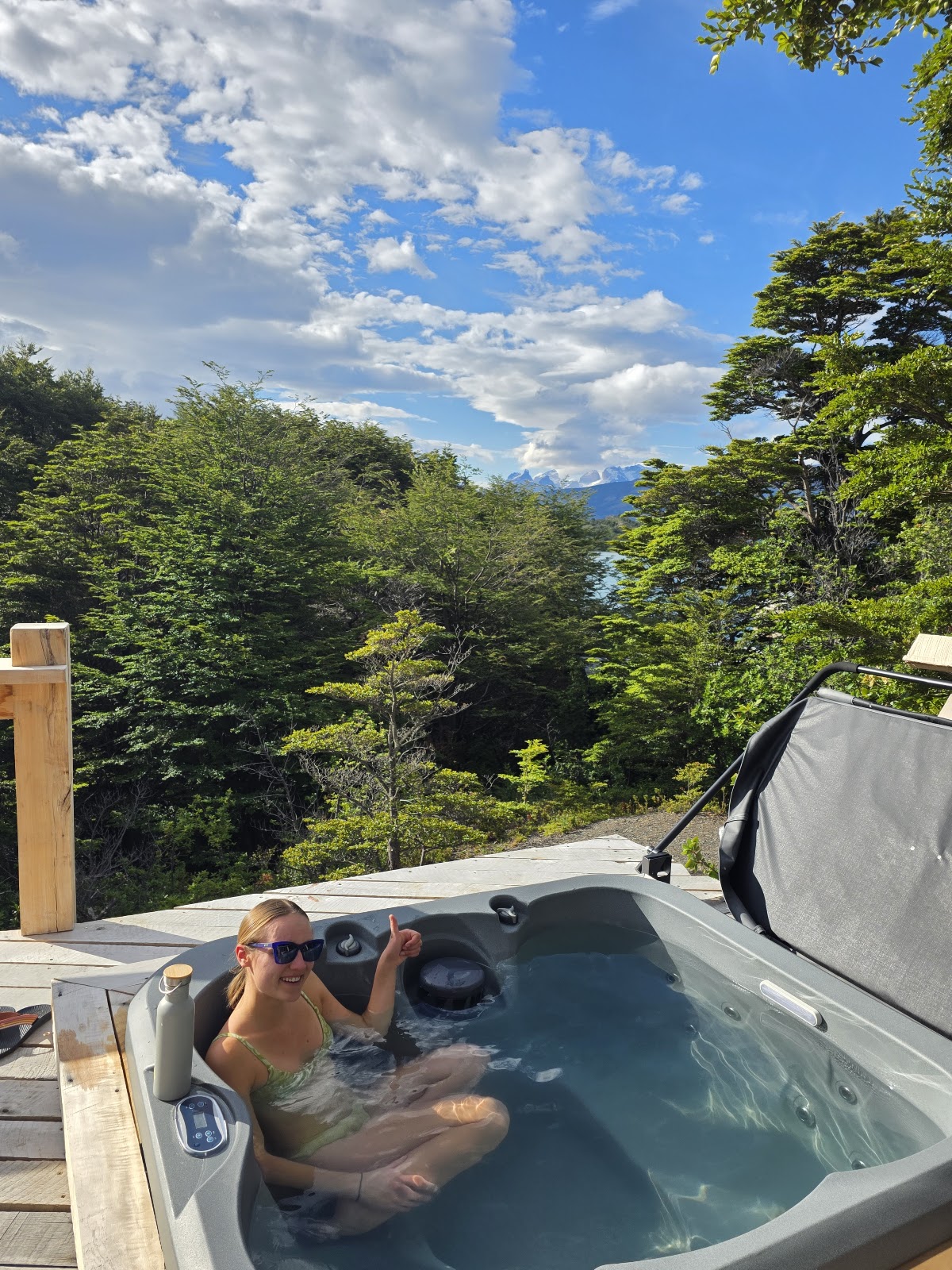 Woman relaxes in outdoor hot tub overlooking dense forest and distant mountains at Patagonia Camp.